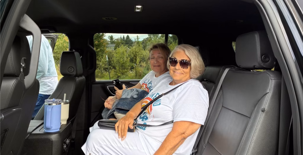Two smiling women sitting in the leather back seat of a spacious black SUV looking toward the camera.