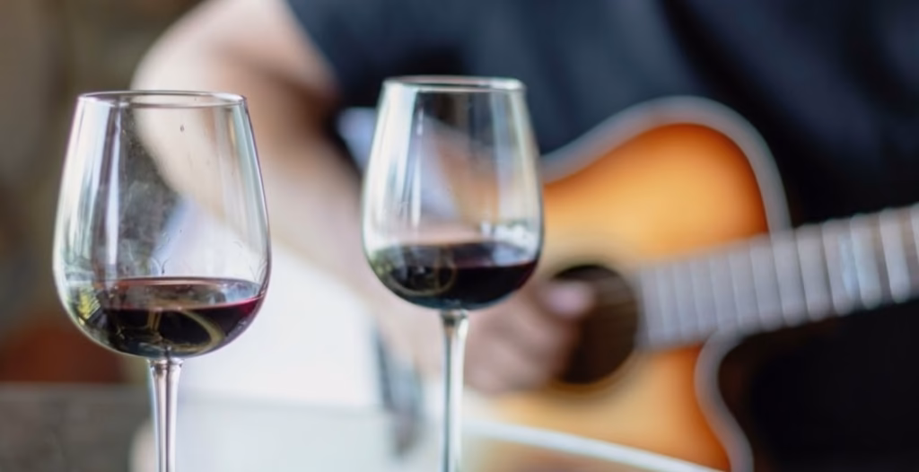 Woman with curly hair in a black sweater smelling red wine in a glass.