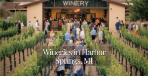 Crowd walking through vineyard rows toward a winery building with overlay text: Wineries in Harbor Springs, MI.
